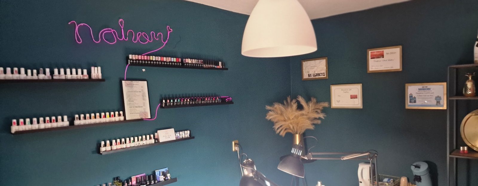 De studio van NaHomi: donkergroene muren, rekken vol gelpolish, ingelijste certificaten en de roze neonnaam Nahomi